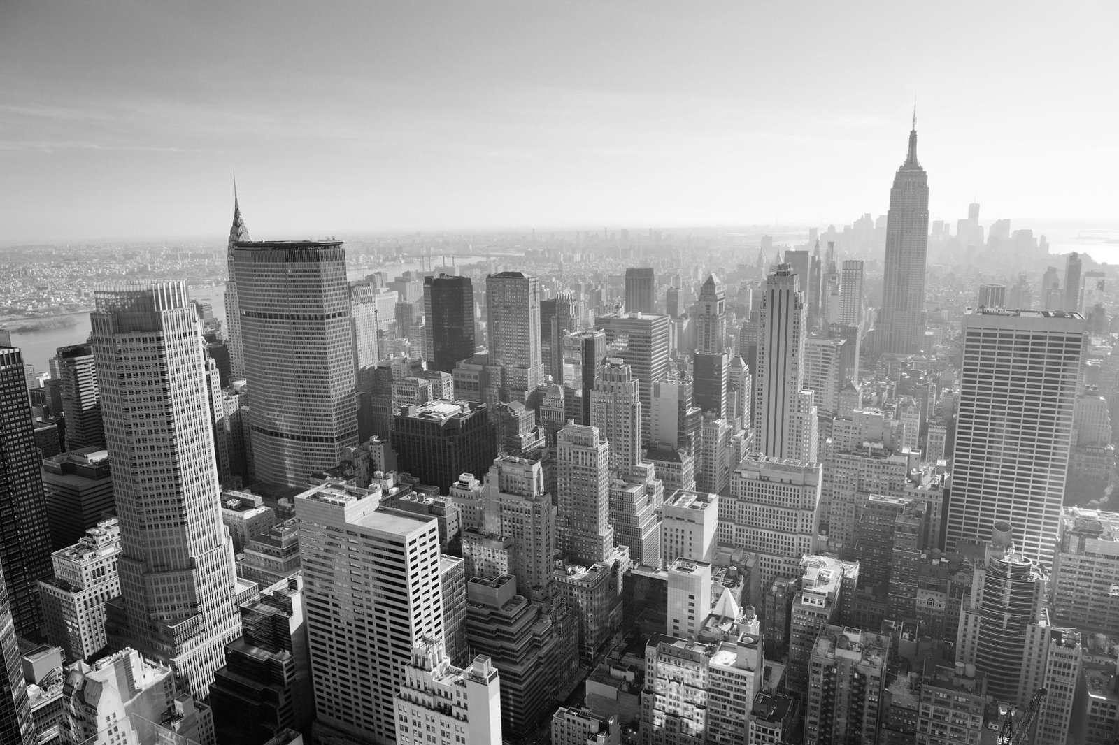 Black-and-white aerial view of Manhattan’s dense skyline, featuring the Empire State Building, towering skyscrapers, and a busy urban cityscape.