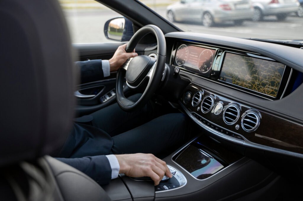 Luxury car interior with driver at the wheel, touchscreen navigation, digital dashboard, and polished controls creating a sophisticated atmosphere.