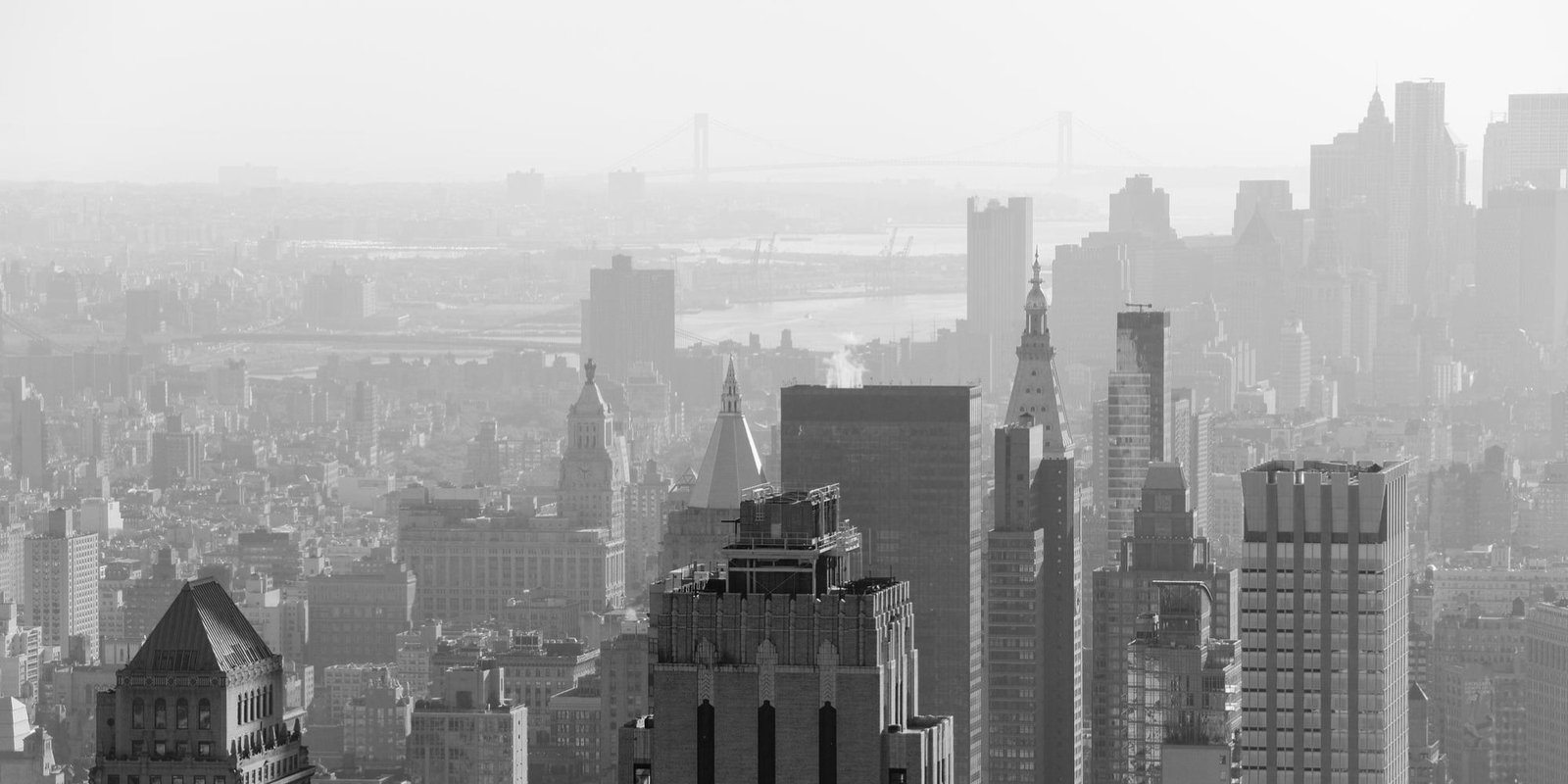 Black-and-white panorama view of Queens’s dense skyline, with skyscrapers in the foreground, bridges and a hazy waterfront beyond.
