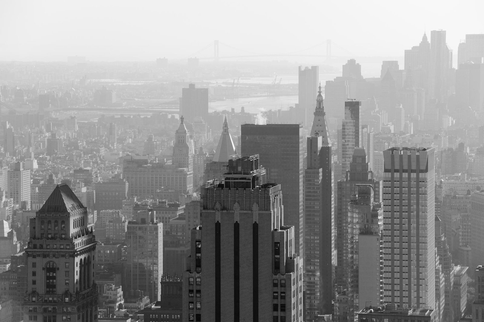 Black-and-white panoramic view of Queens’s dense skyline, with skyscrapers in the foreground, bridges and a hazy waterfront beyond.
