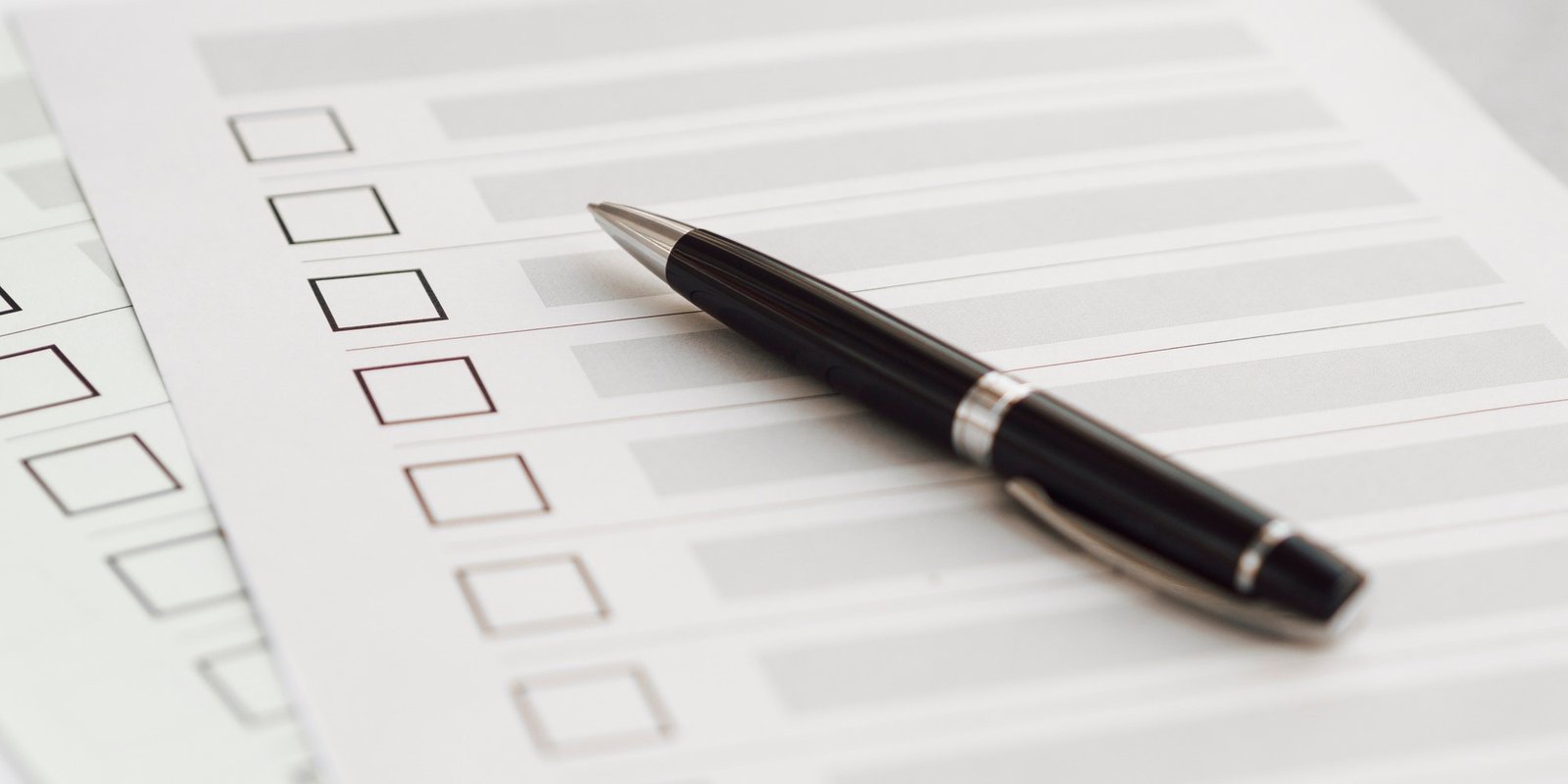 Close-up of a black fountain pen resting on a blank checklist form with empty square boxes and lined fields, suggesting planning and organization.
