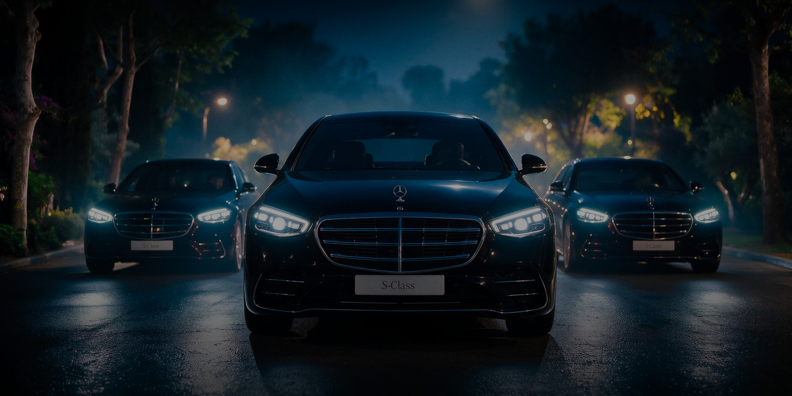 Three black Mercedes-Benz sedans line up on a wet road at night, headlights glowing beneath trees and streetlights in a sleek, dramatic scene.