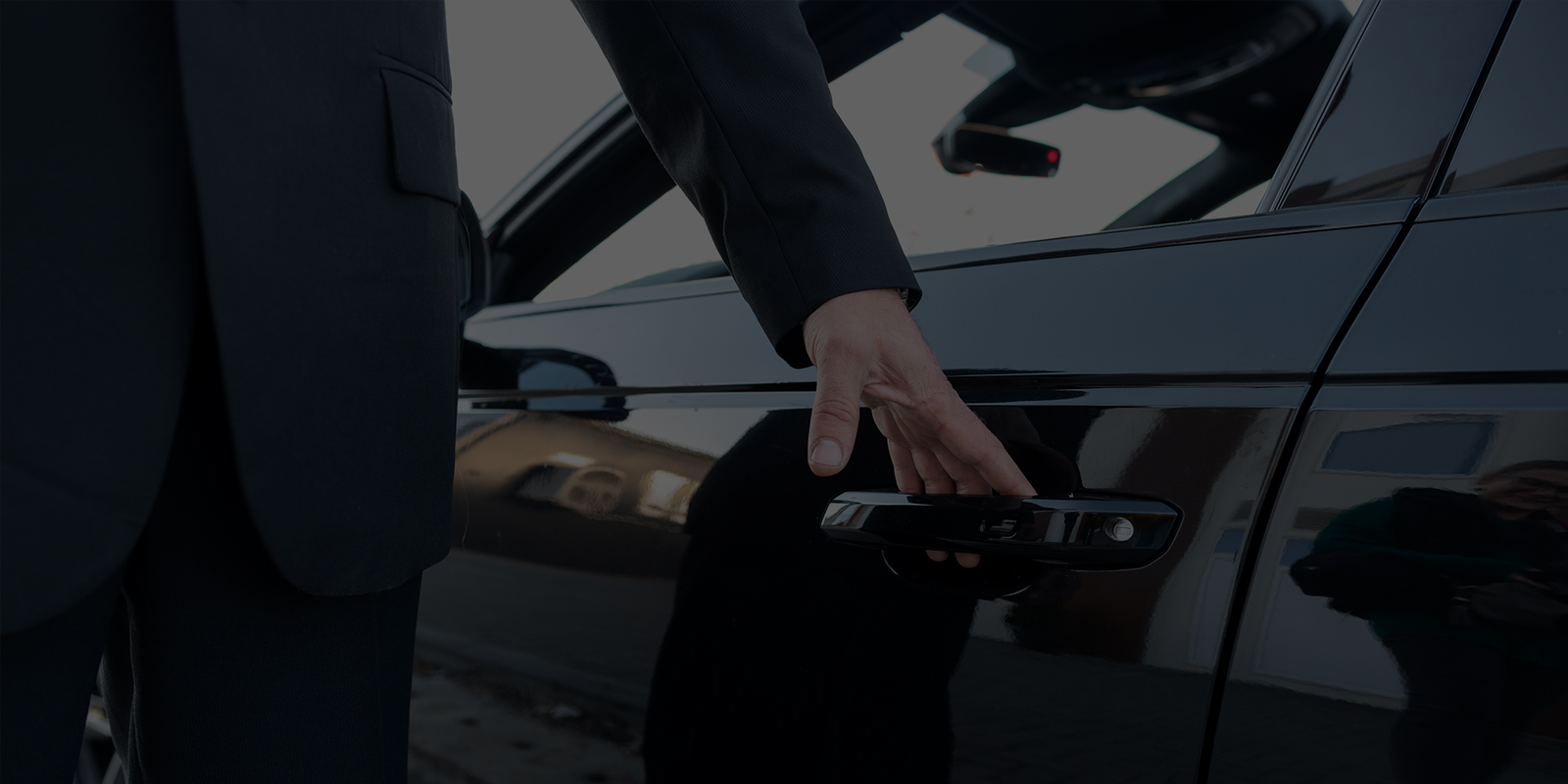Close-up of a chauffeur in dark clothing reaching for a sleek black car door handle, highlighting keyless entry and modern automotive design.