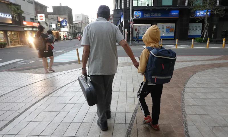 Adult walking a child with a school backpack along a city sidewalk